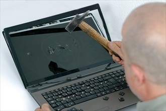 Angry man seen in profile breaking a laptop with a hammer