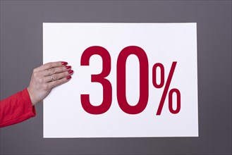 Female hand holding a 30% poster. Studio shot. Commercial concept