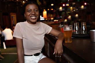 Portrait of smiling young black woman with afro hairstyle looking at camera sitting in a bar