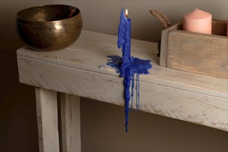 Lighted blue candle melted on a wooden table with a Tibetan bowl in the background and a wooden box with a pink candle