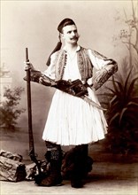 Studio portrait of a man in traditional Greek dress with rifle and sword