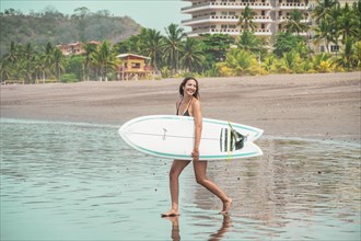 Beautiful young latina with surfboard on the shore walking towards the sea. Holiday and summer concept. Concept of healthy and active life