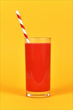 Full glass with red juice and striped drinking straw in front of yellow background