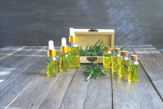 Bottles in a row with droppers of rosemary essential oil with a wooden box and fresh rosemary branches
