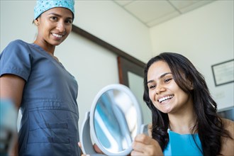 Happy female patient looking at her smile in hand mirror in the presence of her dentist. Concept of whitening