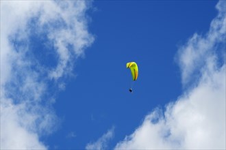 Tandem paraglider high in the slightly cloudy sky