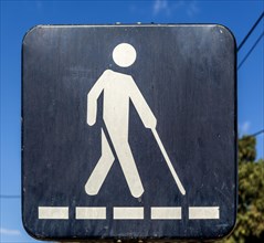 Street sign of blind person crossing road with white stick