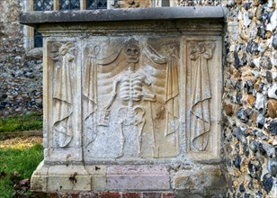 Stone image of skeleton on side of grave tomg in churchyard