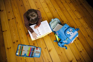 Symbolic photo on the subject of doing homework at home. A boy sits on the floor doing homework. Berlin
