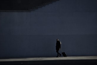 A man with a suitcase stands out in the sunshine at the Spreebogen in the government district in Berlin