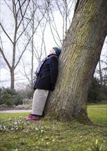 Subject: Pensioner leaning against a tree