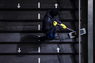 A cleaner wipes a staircase marked with arrows for the respective walking directions