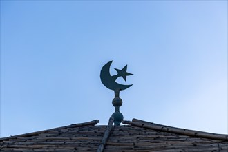 Cresecent moon and star symbol on roof against blue sky