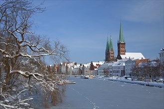 The churches of Saint Petri and Saint Mary towering above historic houses along the frozen river Trave in Luebeck in winter