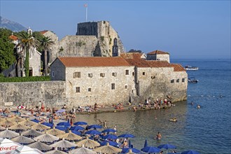 Pebble beach with sunbathers in summer outside the Venetian city walls of Budua at the medieval town Budva along the Adriatic Sea
