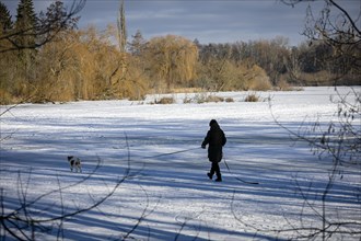 A woman walks her dog across the ice on the frozen Hermsdorfer See lake in Berlin Reinickendorf. Berlin
