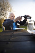 Subject: Pensioner pours himself a glass of red wine