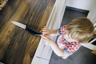 Symbol photo on the subject of dangers in the home. A small child reaches for a knife in the kitchen at home. Berlin