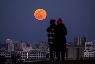 The rising full moon stands out behind the city view of Berlin