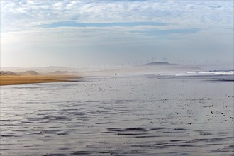 Silhouette figure man running in the distance on wide sandy beach at low tide