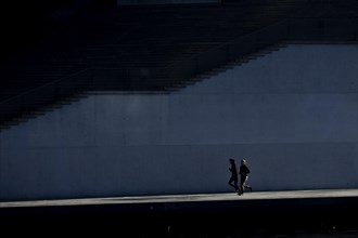 Two joggers stand out in the sunshine at the Spreebogen in the government district in Berlin