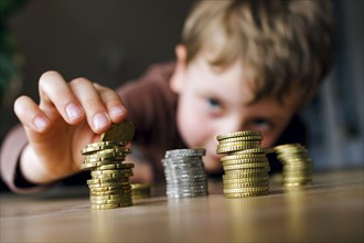 Symbolic photo on the subject of saving money in childhood. A five-year-old boy stacks small change on a table. Berlin