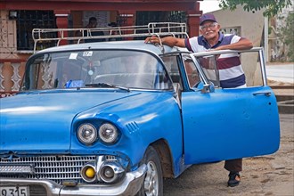 Cuban taxi driver posing with blue American classic car taxi in the city Florida