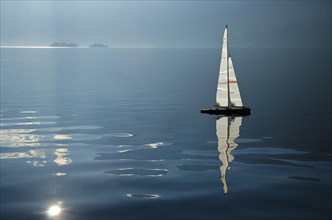 Sailing boat on an alpine lake Maggiore with Brissago islands and reflections in Ticino