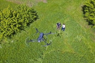 Rescue team operating drone flying over meadow to locate roe deer fawns hidden in grass with thermal imaging camera before mowing grassland in spring