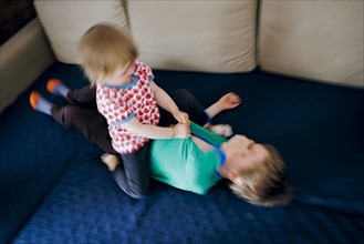 Symbolic photo on the subject of quarrels between siblings. A two-year-old girl and a five-year-old boy fight on a couch at home. Berlin