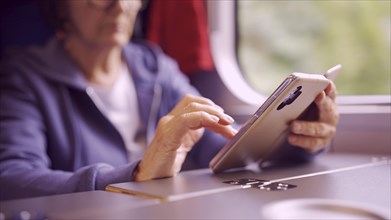 Close-up of the hands of an elderly woman sitting in a train carriageriage and using a smartphone