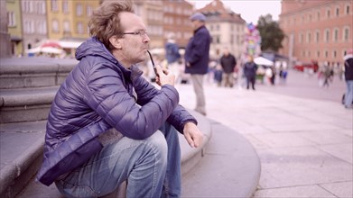 Adult man sitting on square and smoking a tobacco pipe in the Palace Square