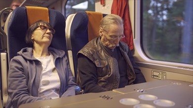 An elderly couple ride the train early in the morning and sleep