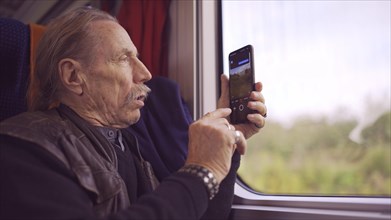 Elderly man traveling by train and taking pictures of the landscape through the window using a smartphone