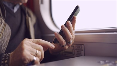 Close-up of the hands of an senior sitting in a train carriageriage and using a smartphone