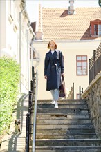 Redhead woman in blue trench coat and sneakers descending stairs