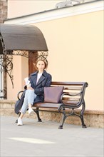 Stylish red head businesswoman in trench coat and coffee cup sitting on bench