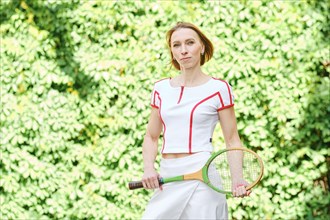 Adult redhead woman in tennis outfit posing with tennis racket