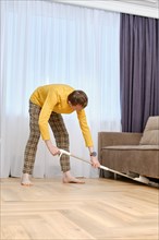 Single middle age man mopping floors under the sofa