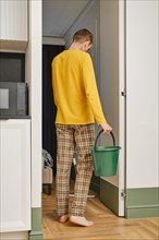 Back view of middle age man with mop and bucket entering bedroom