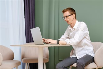 Middle aged man in casual white shirt and grey trousers working online at home