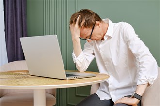 Upset and tired middle aged man with laptop lower his head
