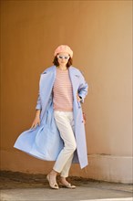 Playful woman standing in arch and waiving her blue trench coat