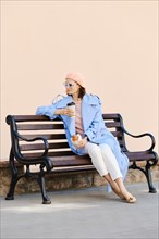 Woman sitting on bench with coffee and croissant and looking to the side