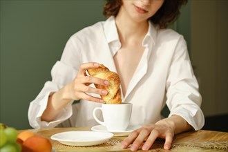Unrecognizable woman dipping croissant into cappuccino