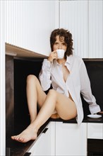 A stunning brunette enjoys coffee while sitting in the kitchen