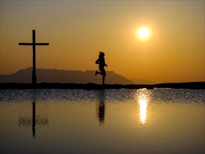 Silhouette of a runner with summit cross at sunset
