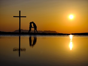 Couple kissing next to summit cross at sunset