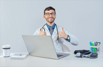 Smiling doctor sitting with laptop giving thumbs up