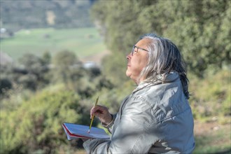 Woman with a notebook and a pencil in her hand in the field looking at the horizon thinking